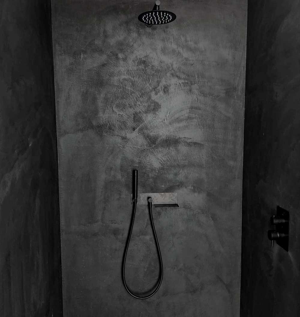 Black microcement shower with shower head and handheld shower on a textured microcement wall.