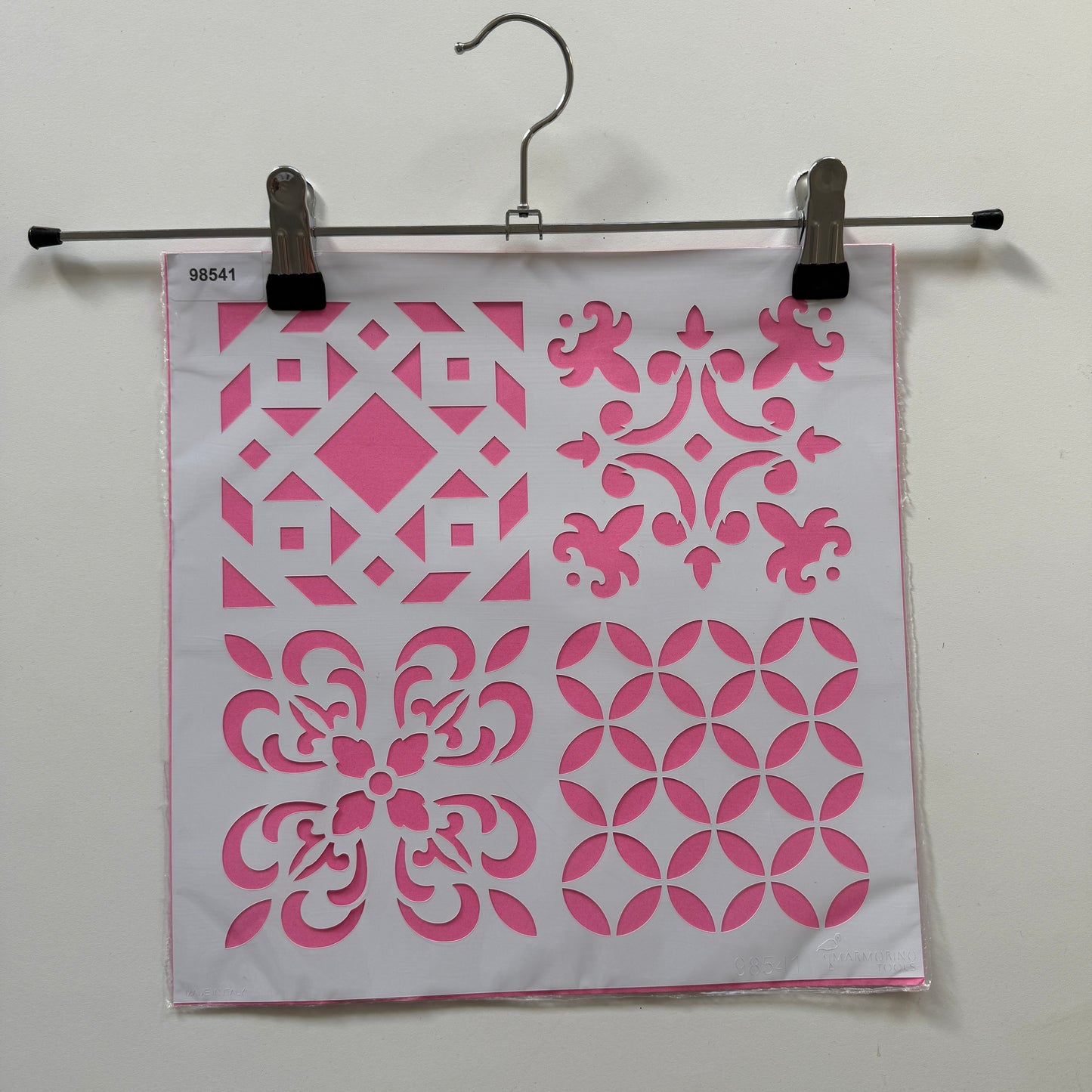 Pink and white geometric patterned reuseable stencil  binder clip on a white background