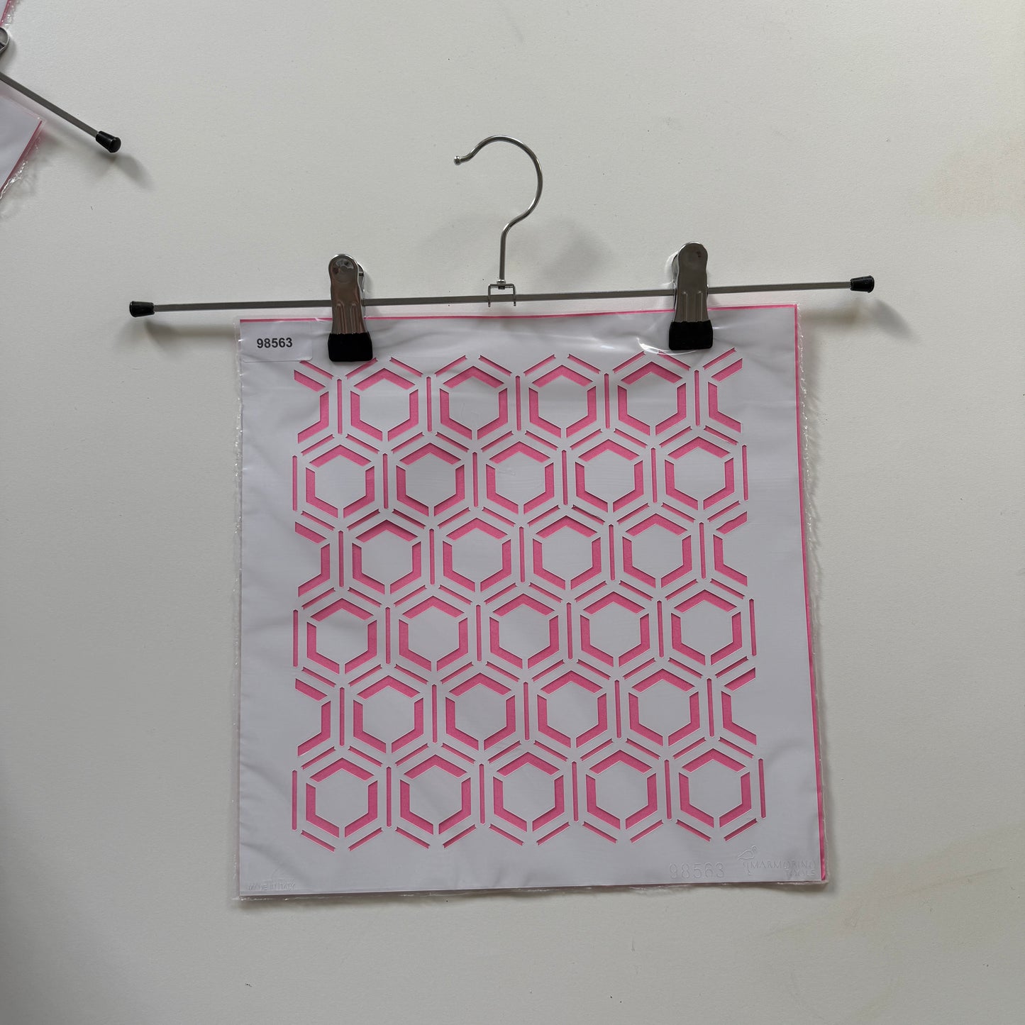 Pink and white geometric patterned reuseable stencil  binder clip on a white background