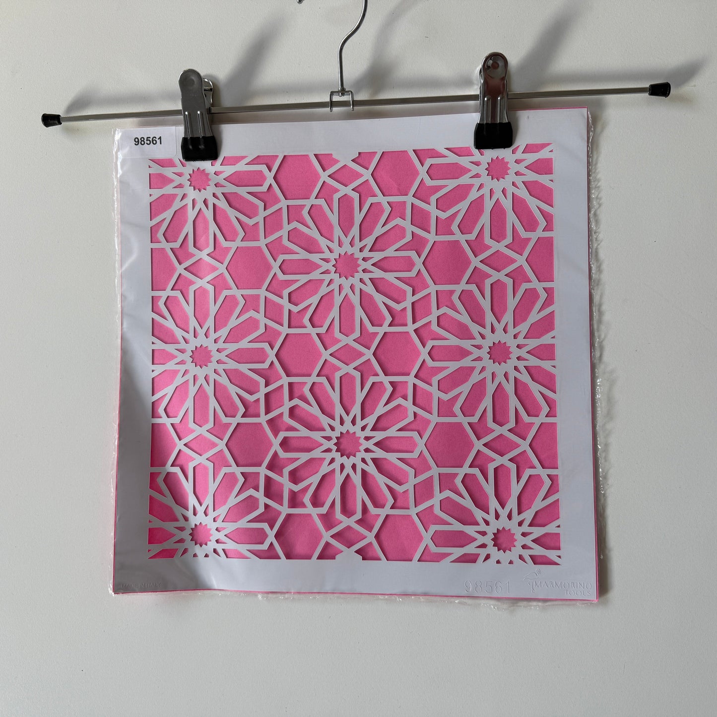 Pink and white geometric patterned reuseable stencil  binder clip on a white background