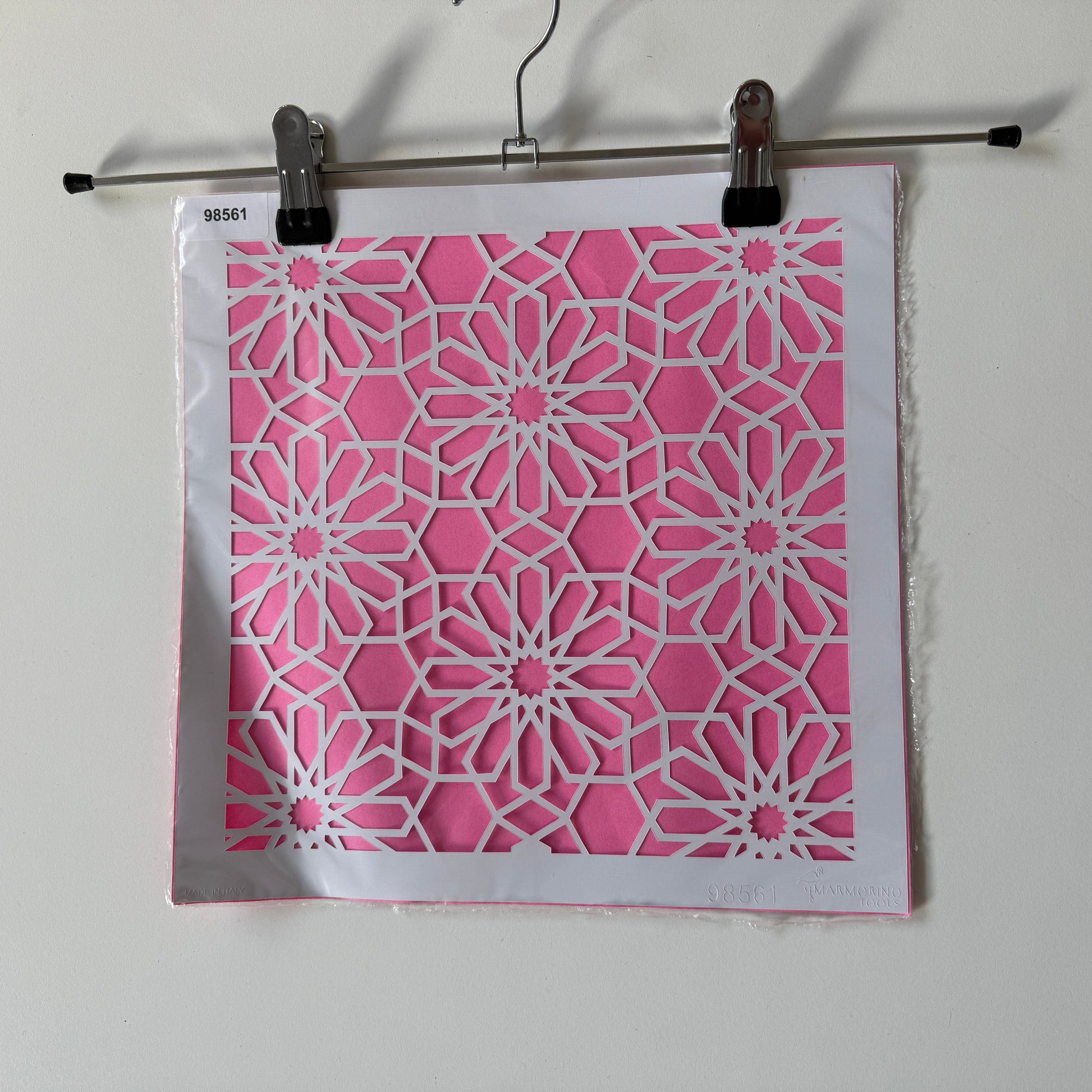 Pink and white geometric patterned reuseable stencil  binder clip on a white background