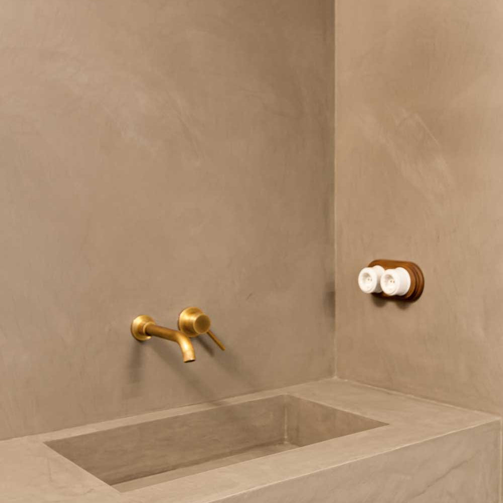 Microcement Bathroom sink with gold faucet and toiletries against a beige wall.