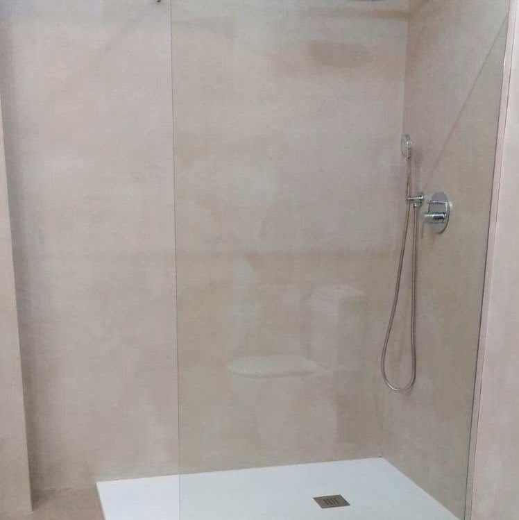 Shower enclosure with a glass door and microcement walls in a bathroom setting.